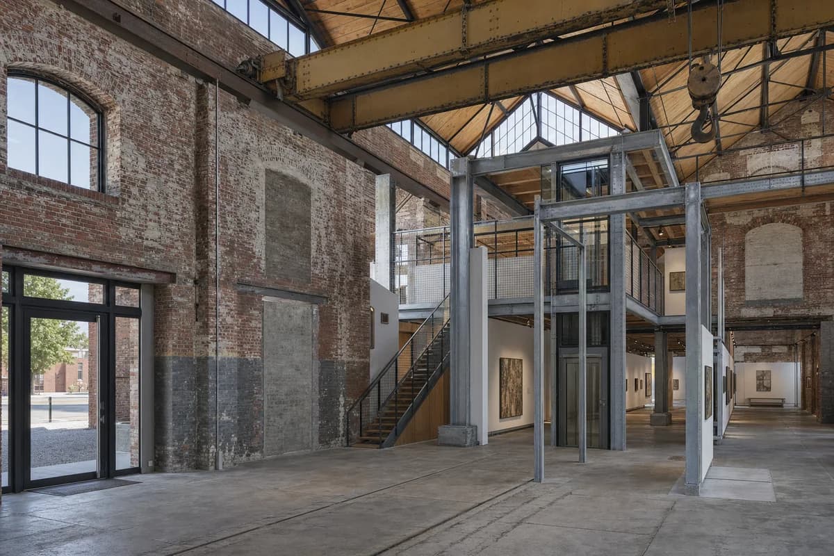 Unoccupied foundry museum with a reversible steel gallery frame inside patched brick walls.