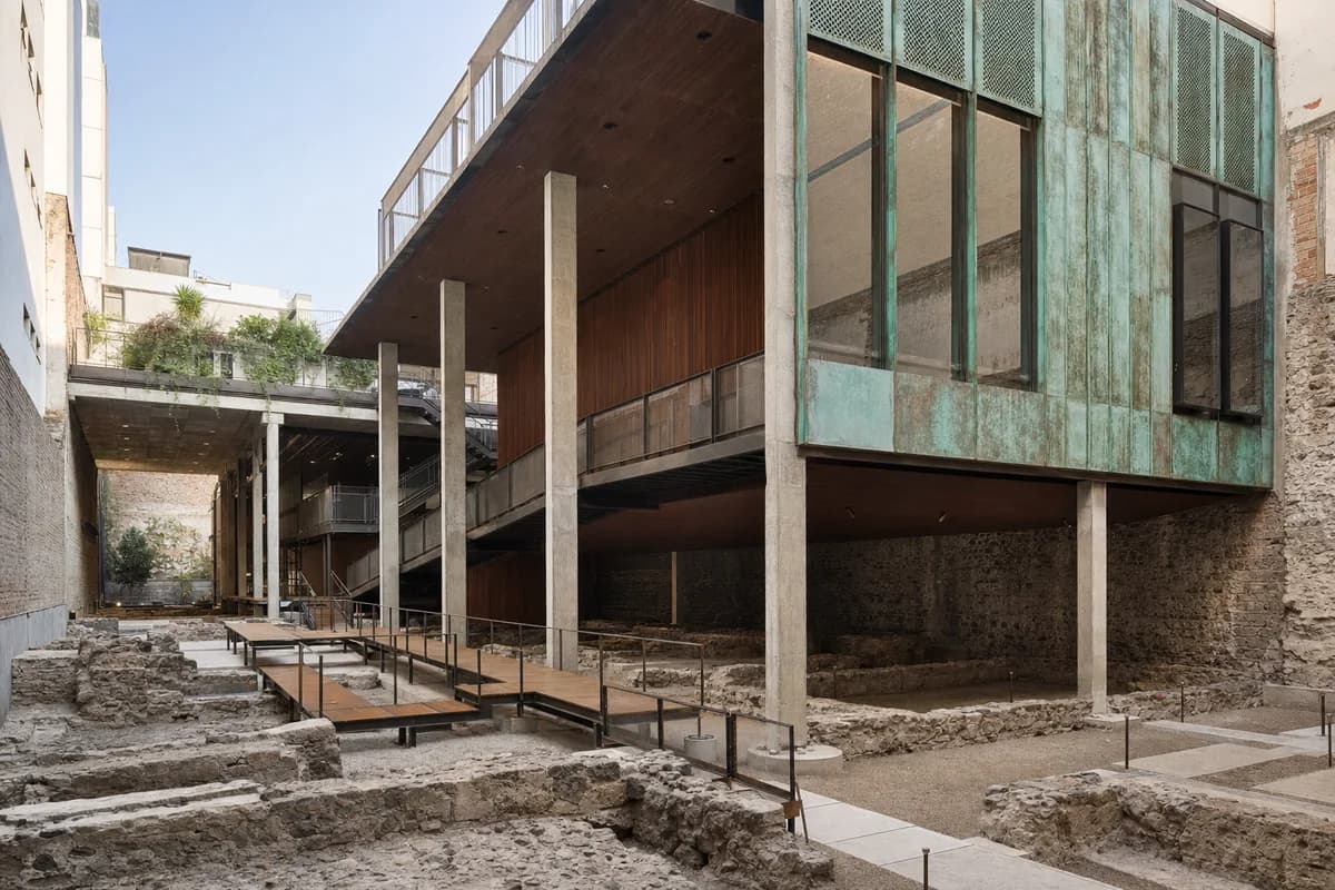 Concrete and copper museum spanning protected urban foundations.