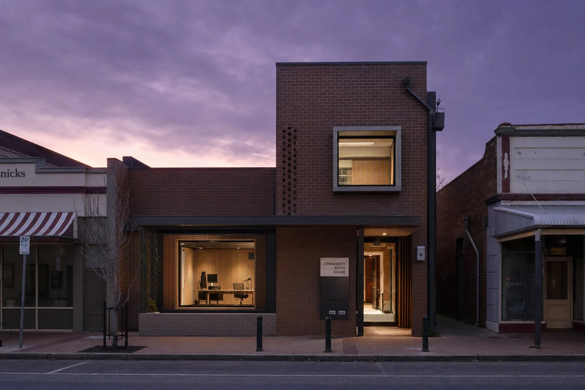 Brick community radio house with one selectively lit studio at violet dusk.