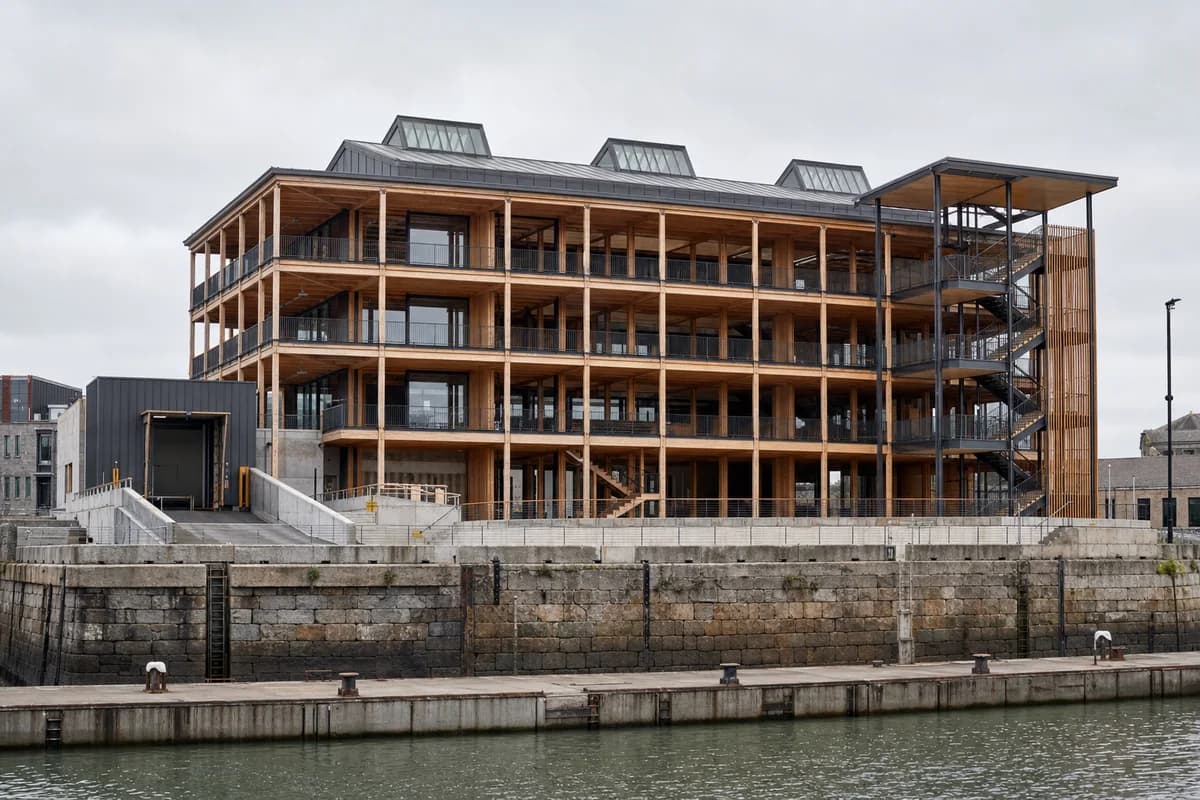 Timber migration museum rising behind a retained stone quay wall.