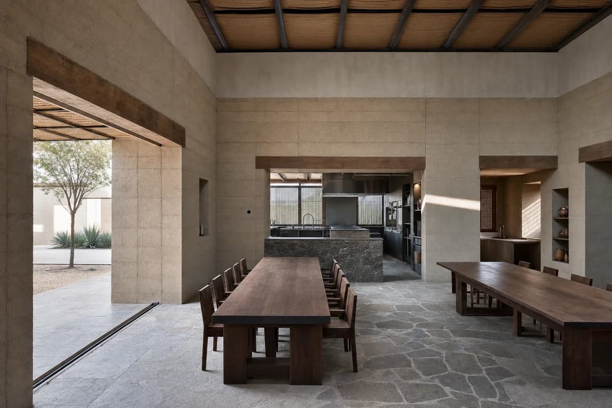 Earth-block tasting room with deep openings, solid timber tables, and a shaded courtyard threshold.