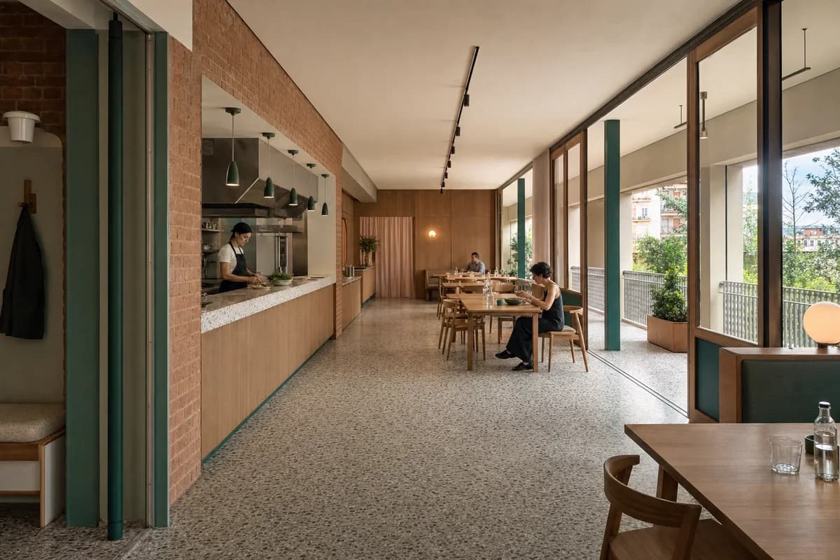 Loggia Community Dining, cooperative eatery organized by a kitchen pass and shared tables aligned with a deep loggia.