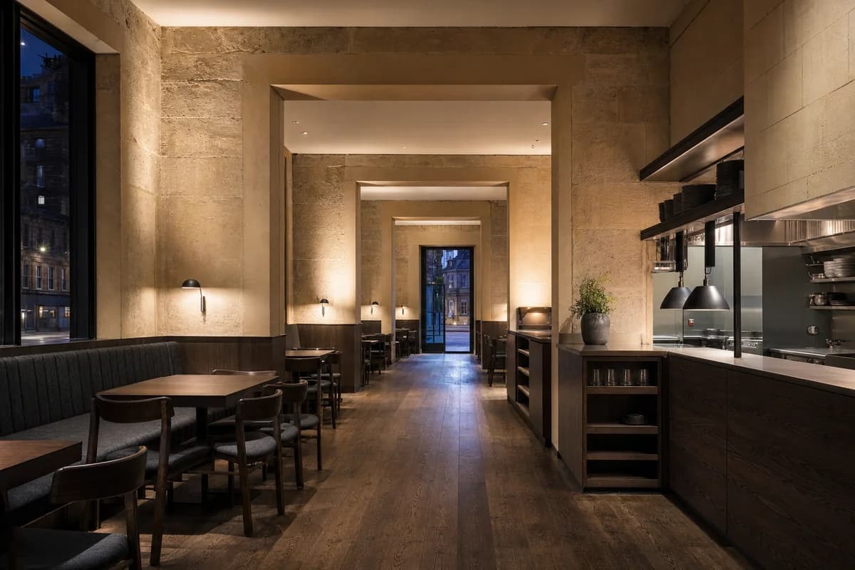 Night Masonry Supper Room, urban restaurant organized by three nested sandstone dining bays opening onto one clearly lit service aisle, with dark-oak banquettes and tables stopping short of every doorway and egress turn.