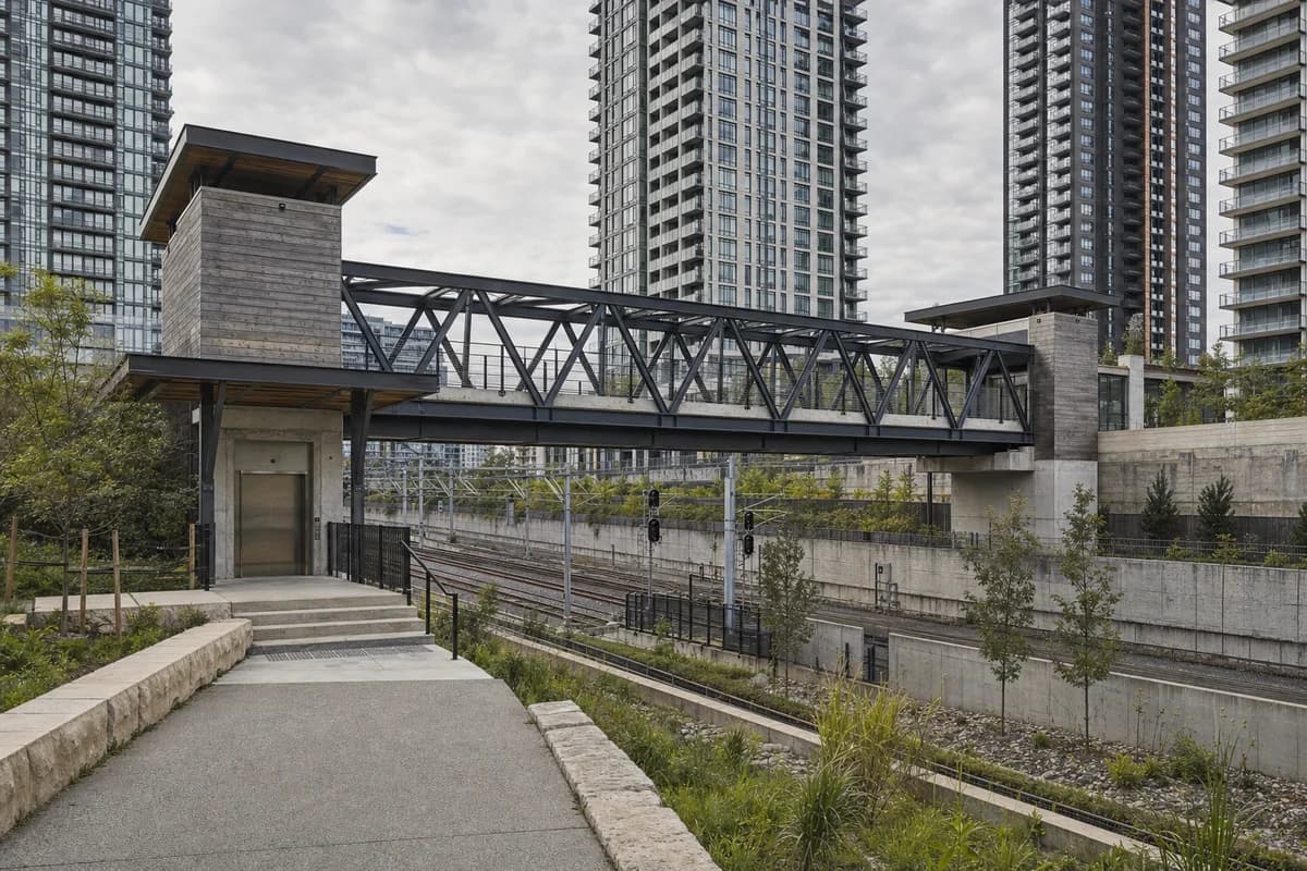 Unoccupied timber and aluminum bridge crossing a rail cut between dense towers.