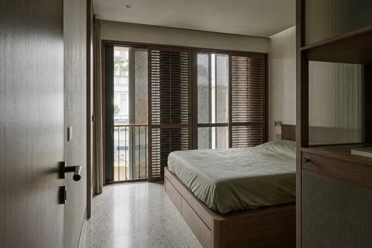 Monsoon Shutter Room, apartment bedroom organized by layered shutters providing privacy, airflow, and a narrow balcony bay.