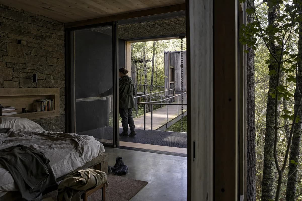 Modest timber bedroom pavilion opening through a screened threshold to managed woodland.