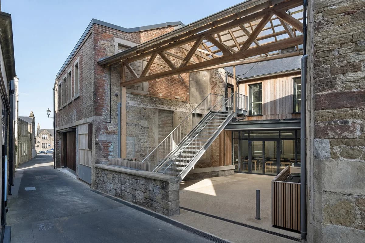 Unoccupied patched-brick mill courtyard with a reversible stair and precise drained junctions.