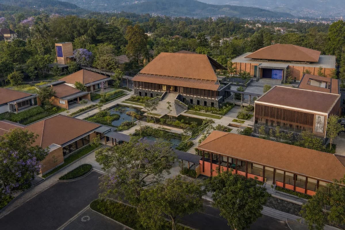 Warm aerial of a colorful Bandung arts campus with terracotta roofs, volcanic stone, and lush rain gardens.