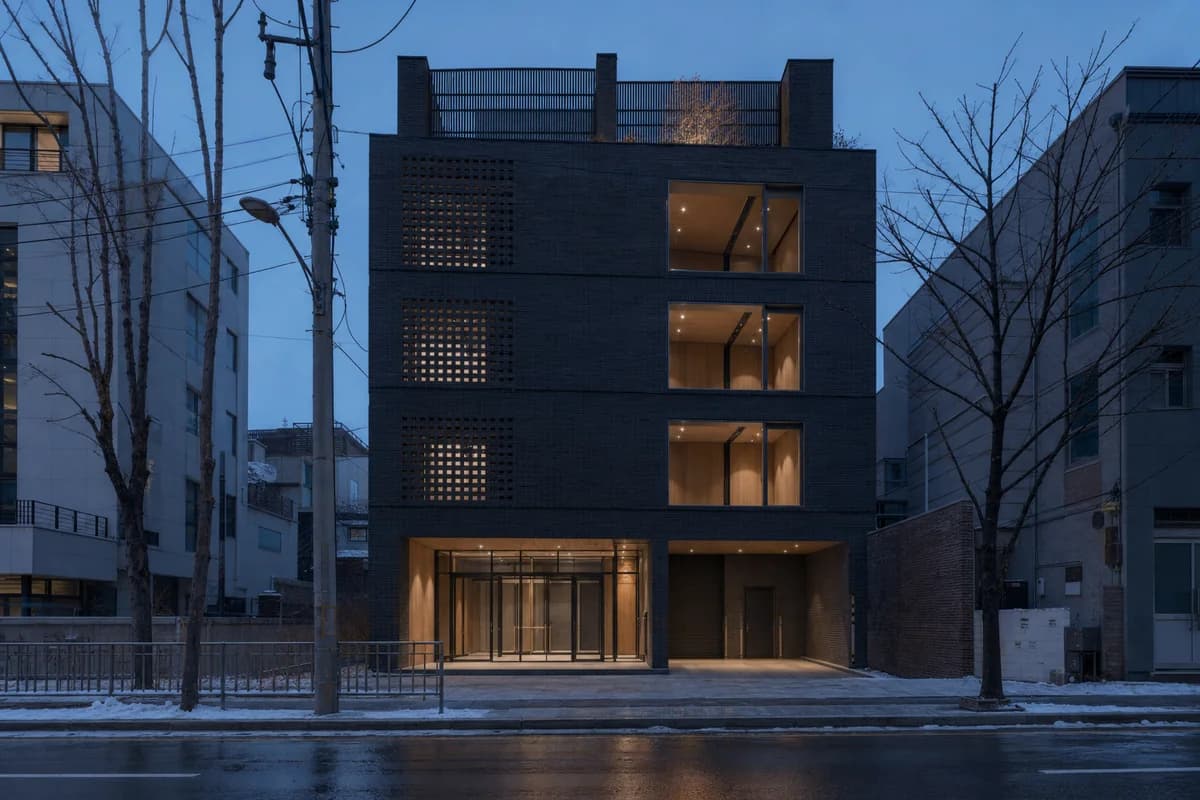 Dark brick rehearsal house with a timber-lit foyer in Seoul.