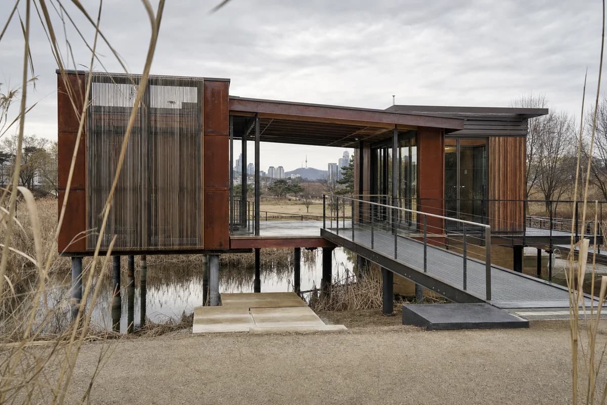 Unoccupied weathering-steel and timber climate gallery seen through a Seoul reed garden.