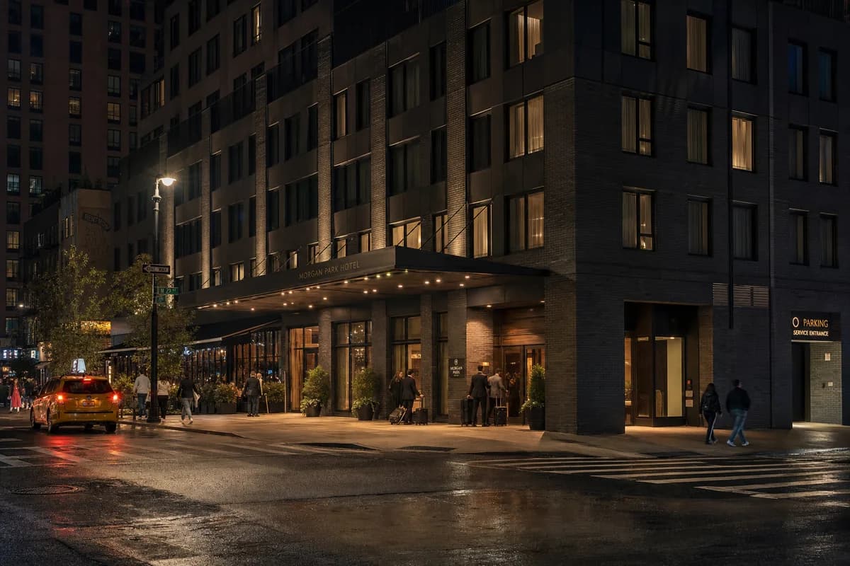 Dark masonry corner hotel with restrained lobby light and active rainy curbside.