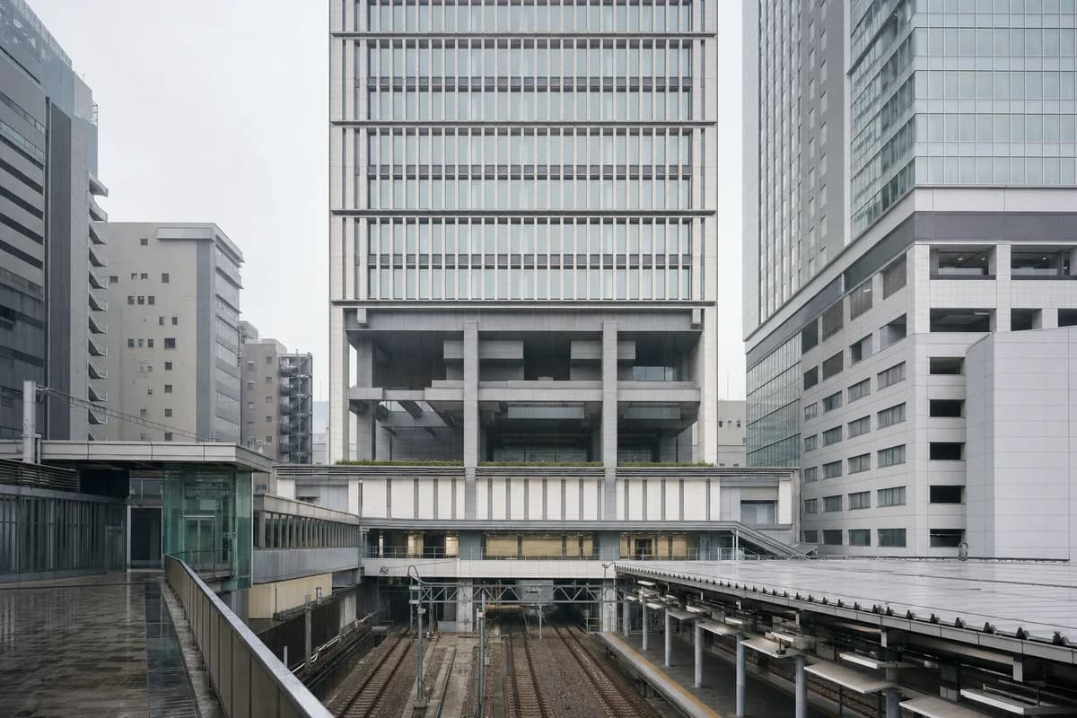 Thirty-storey ceramic-finned office tower with banded floors and a deep transfer structure beside a rainy railway.