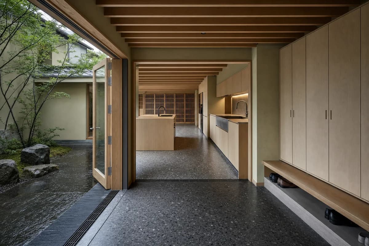 Unoccupied Kyoto courtyard entry kitchen with cedar beams, concealed storage, and a drained terrazzo threshold.