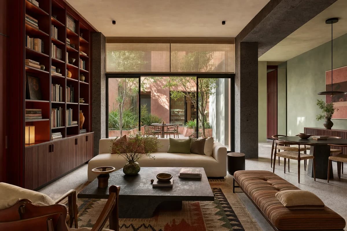 Unoccupied colorful Mexico City living room with volcanic stone, celadon plaster, oxblood joinery, and warm courtyard light.
