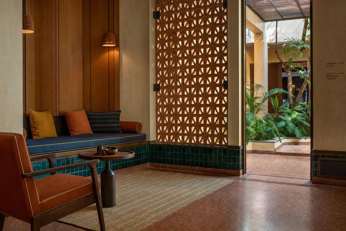 Unoccupied colorful Dakar hotel salon detail with teal tile, iroko panels, woven upholstery, and warm filtered light.
