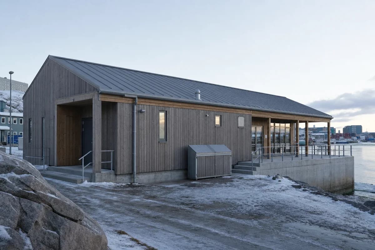 Compact timber community hall beside Nuuk harbor in low winter light.